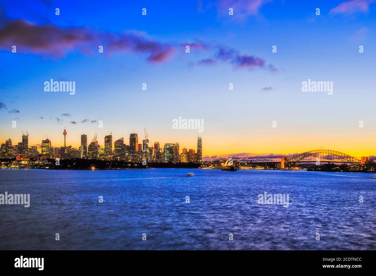 Tramonto blu giallo sullo skyline della città di Sydney attraverso le acque del porto. Foto Stock