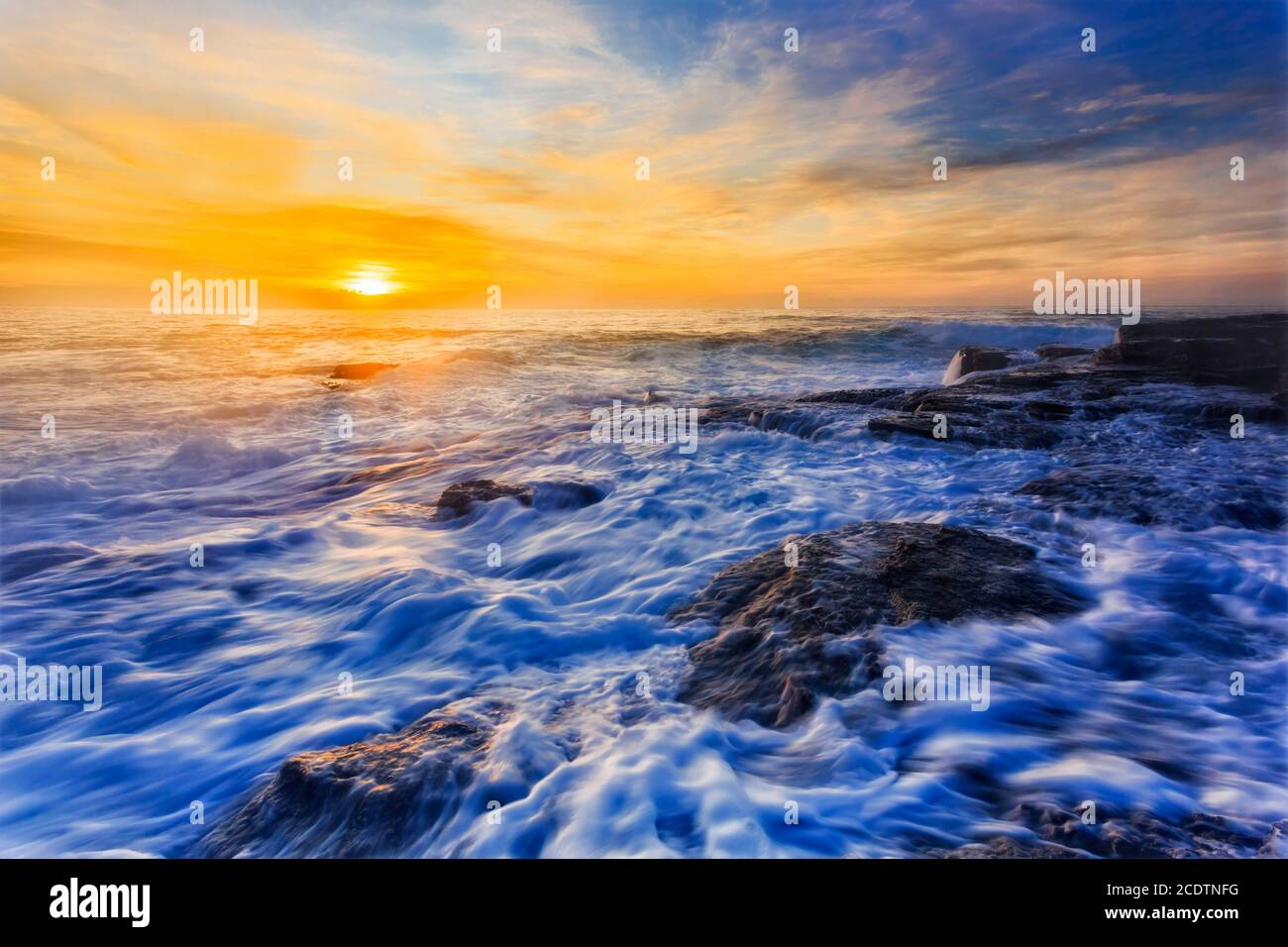 Mare dell'alba dell'oceano Pacifico alle spiagge del nord di Sydney in tempo tempestoso con onde e surf su rocce di arenaria. Foto Stock