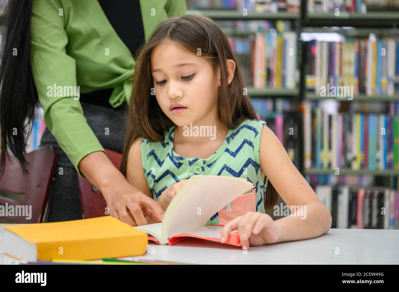 La ragazza chiede all'insegnante di rispondere alla domanda nel libro mentre legge il libro alla biblioteca della scuola. Concetto di istruzione e apprendimento. Foto Stock