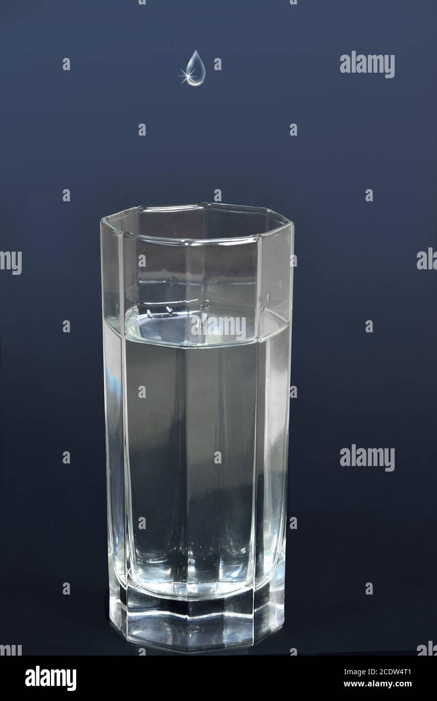 Goccia d'acqua che cade in un bicchiere pieno di bevanda Foto Stock
