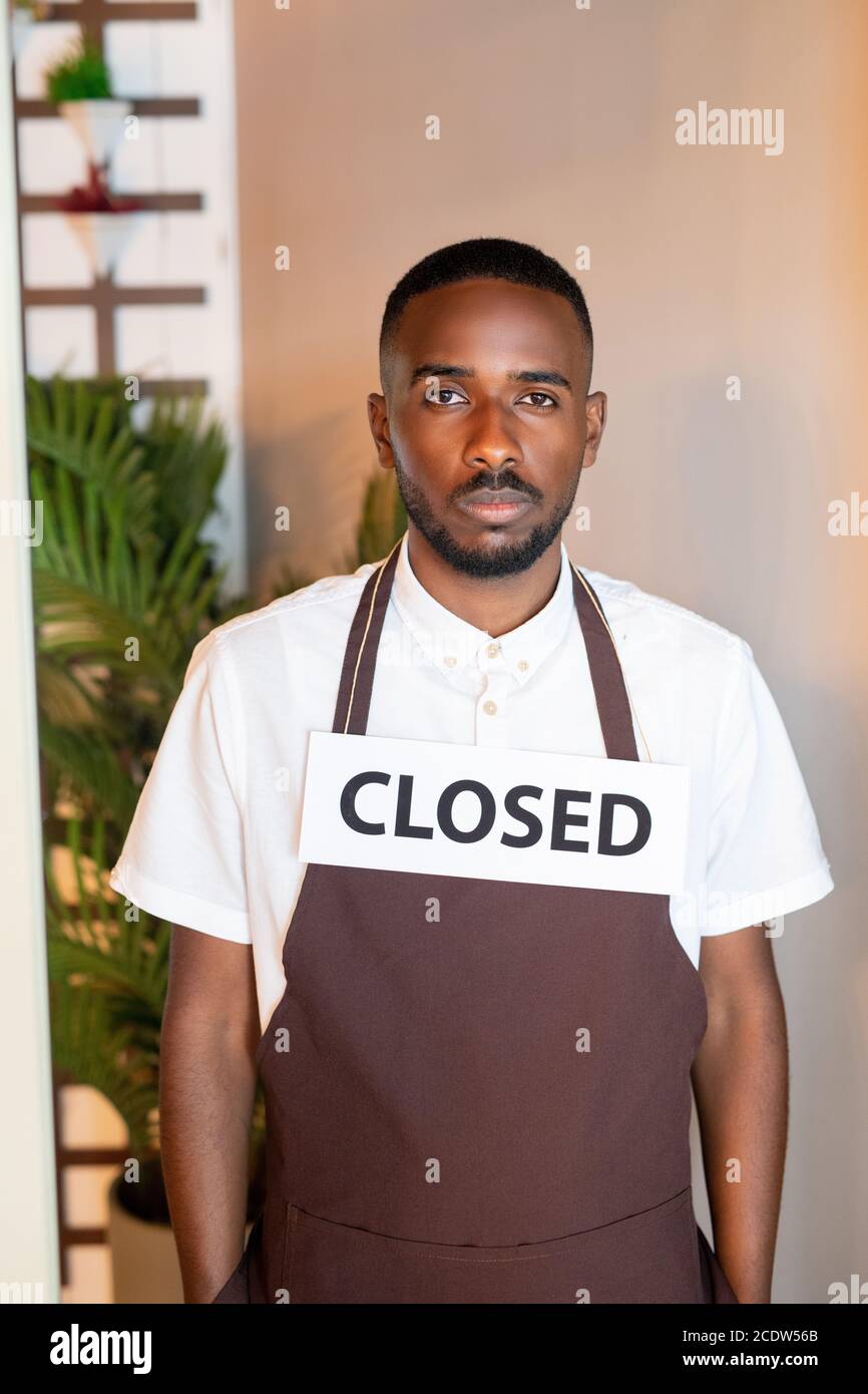 Giovane serio cameriere di etnia africana con la carta dicendo chiuso sul collo Foto Stock