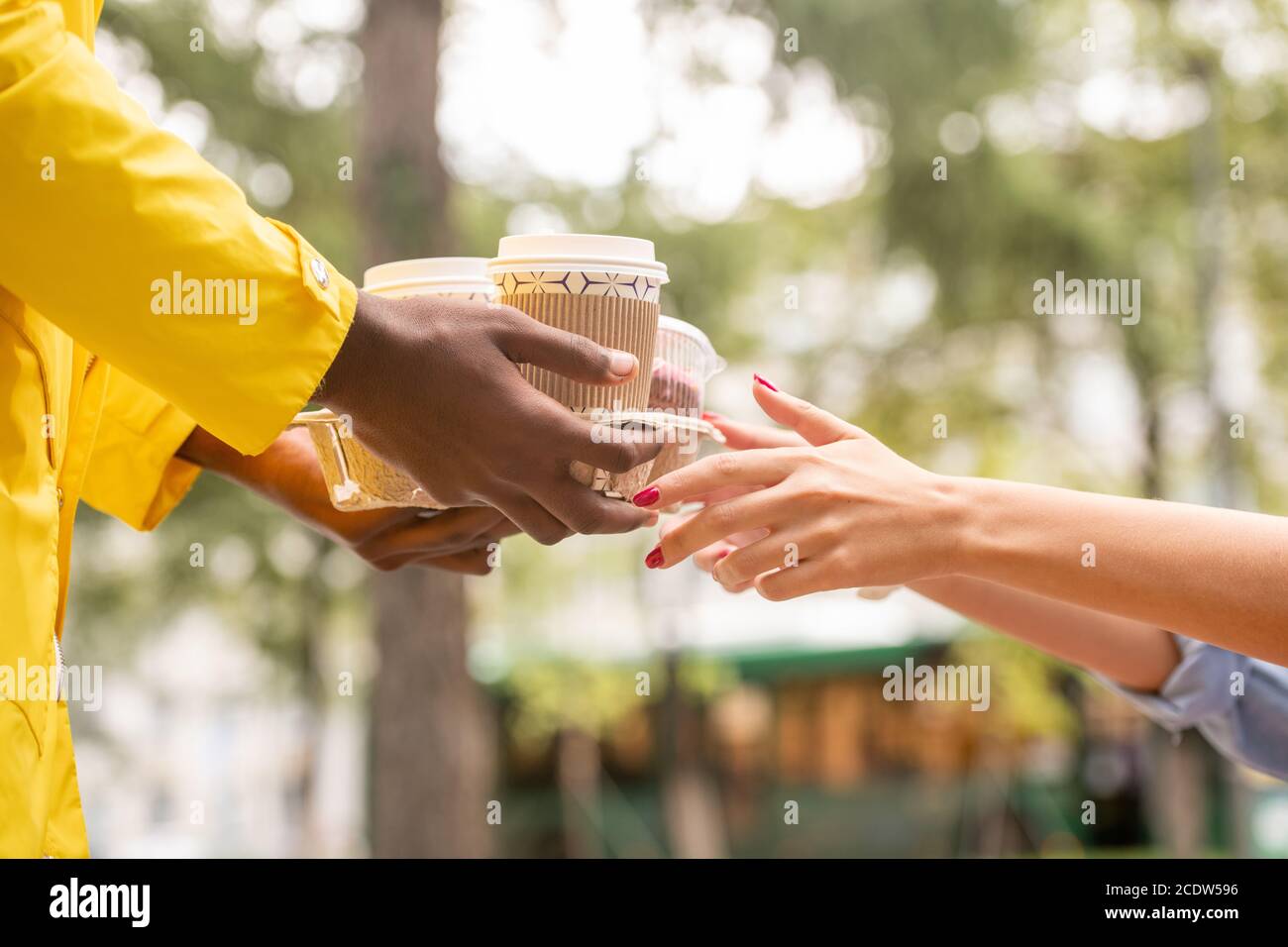 Mani di corriere maschile in uniforme gialla che passa due bicchieri di caffè a donna Foto Stock