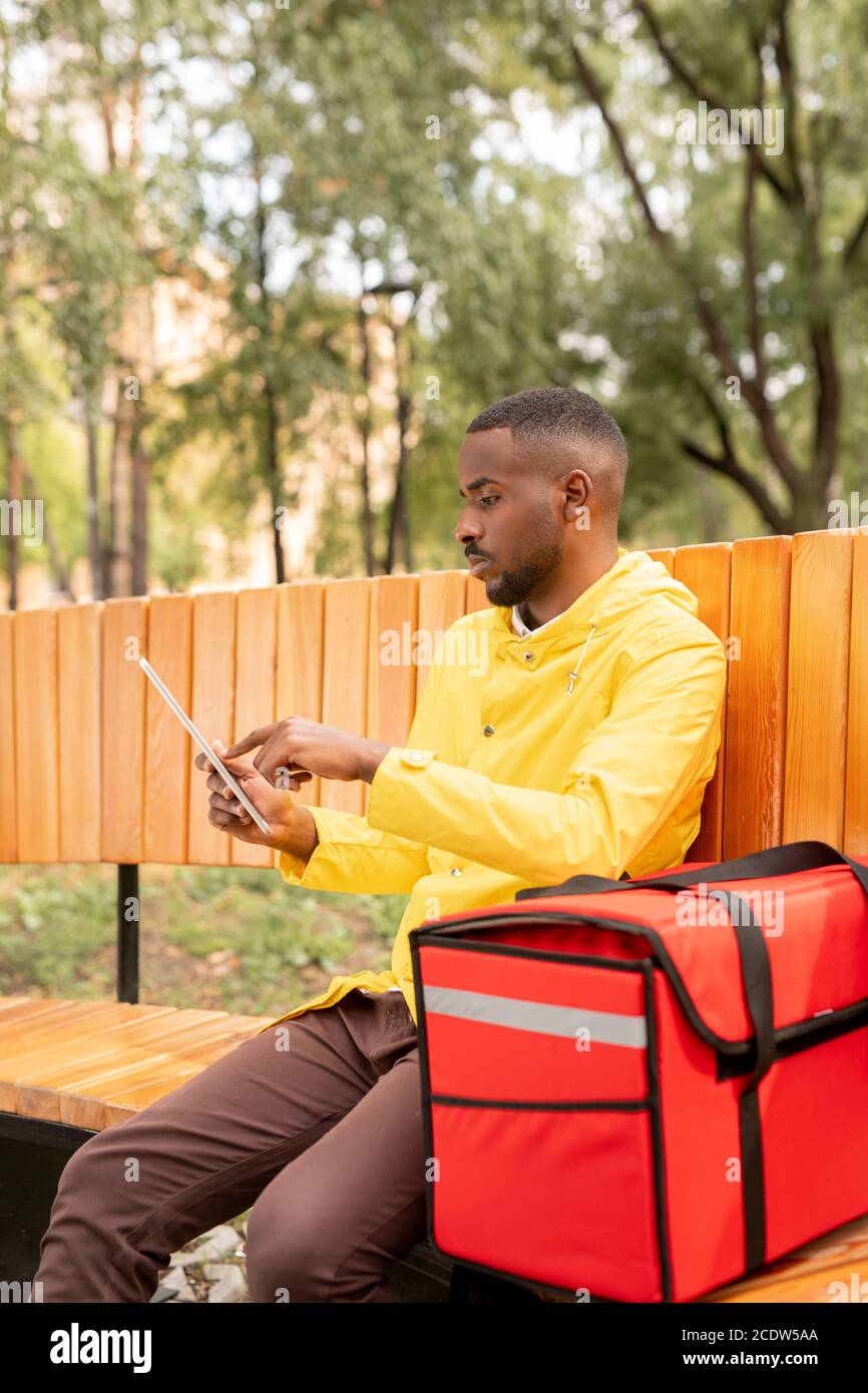 Corriere giovane di etnia africana con grande zaino rosso utilizzando touchpad in posizione di parcheggio Foto Stock