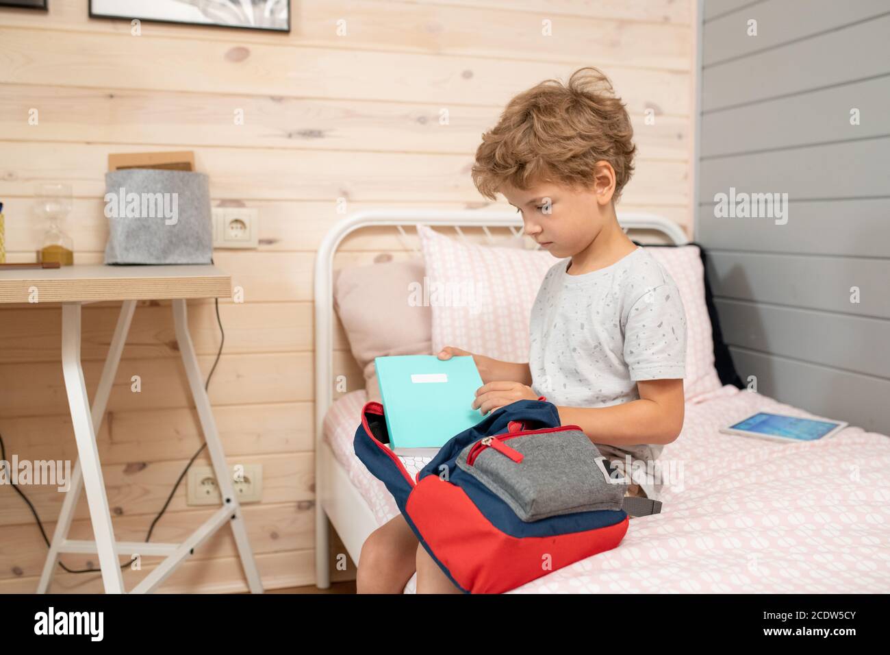 Carino scolaro che raccoglie libri, copybooks e altre cose della scuola in zaino Foto Stock