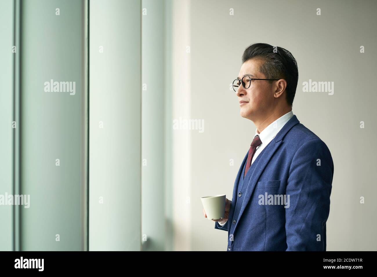 ritratto di un dirigente d'azienda asiatico senior in piedi window thinking Foto Stock