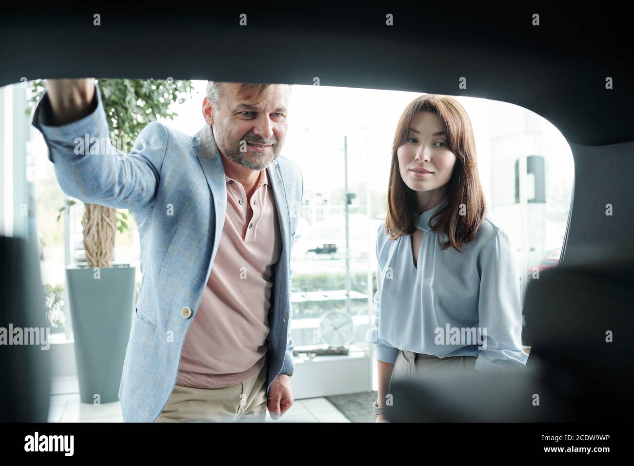Elegante uomo maturo e la sua bella moglie brunette guardando dentro bagagliaio dell'auto Foto Stock