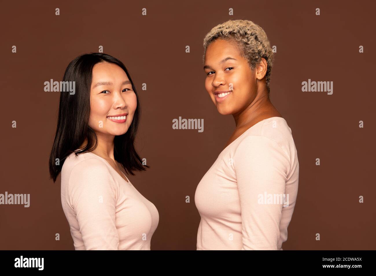Due giovani femmine allegre con sorrisi toothy in piedi di fronte ad una un altro Foto Stock