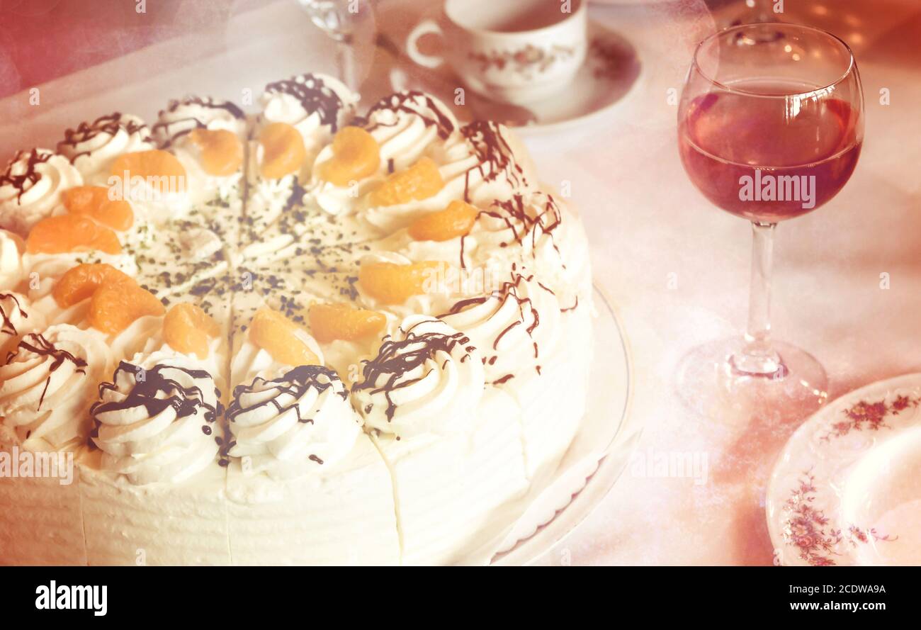 Parte di un tavolino da caffè con torta alla crema di mandarino, bicchiere di vino rosato e stoviglie Foto Stock