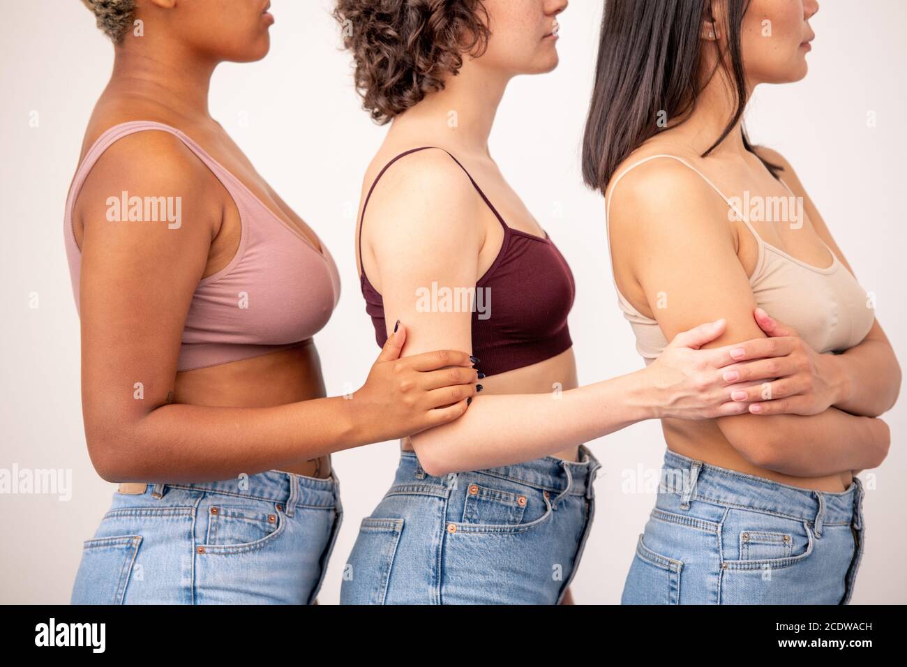 Vista laterale di tre giovani donne di varie etnie in tanktops e jeans blu Foto Stock