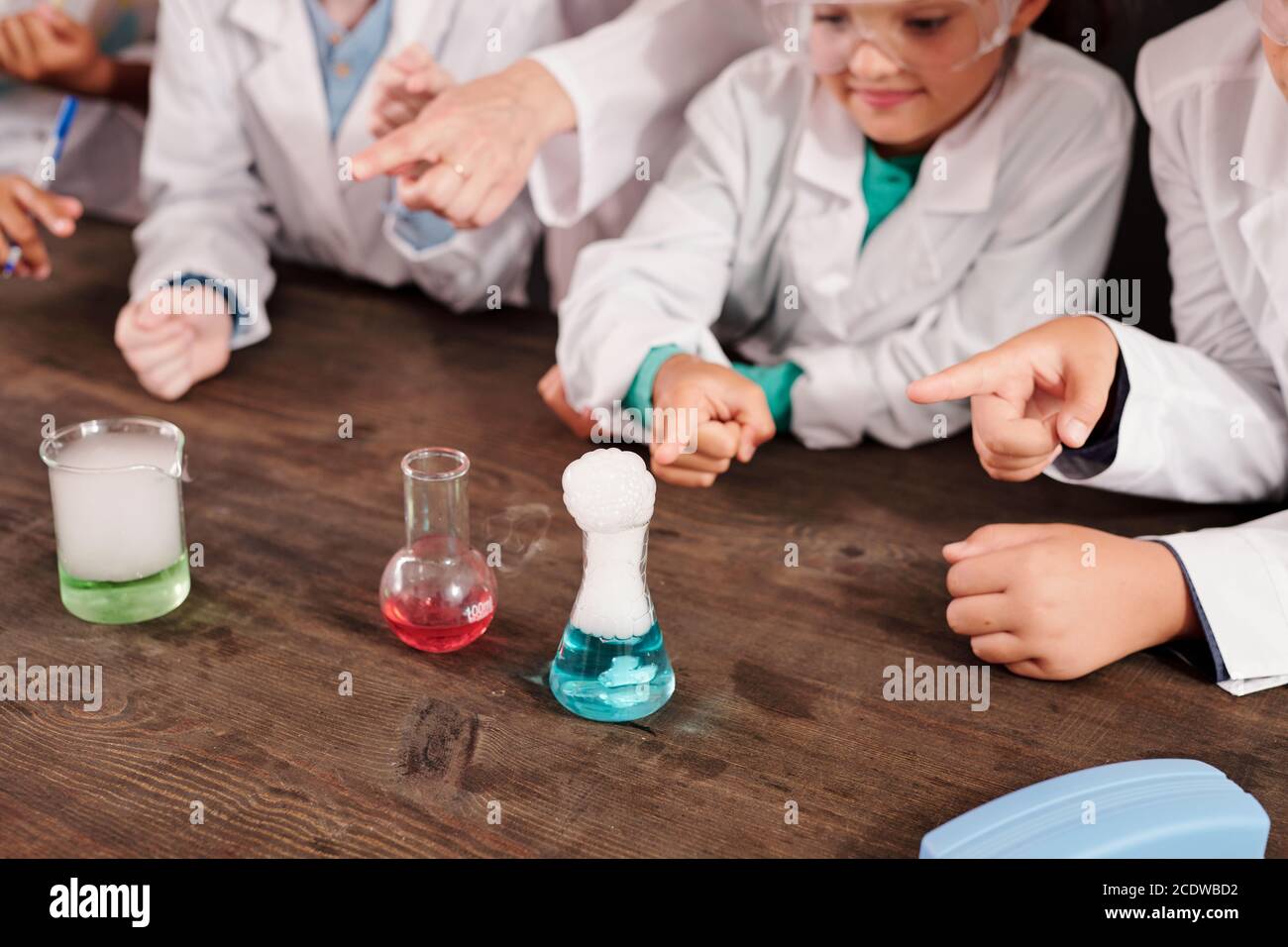 Insegnante di chimica e gruppo di ragazzi in whitecoats che puntano in corrispondenza dei tubi Foto Stock