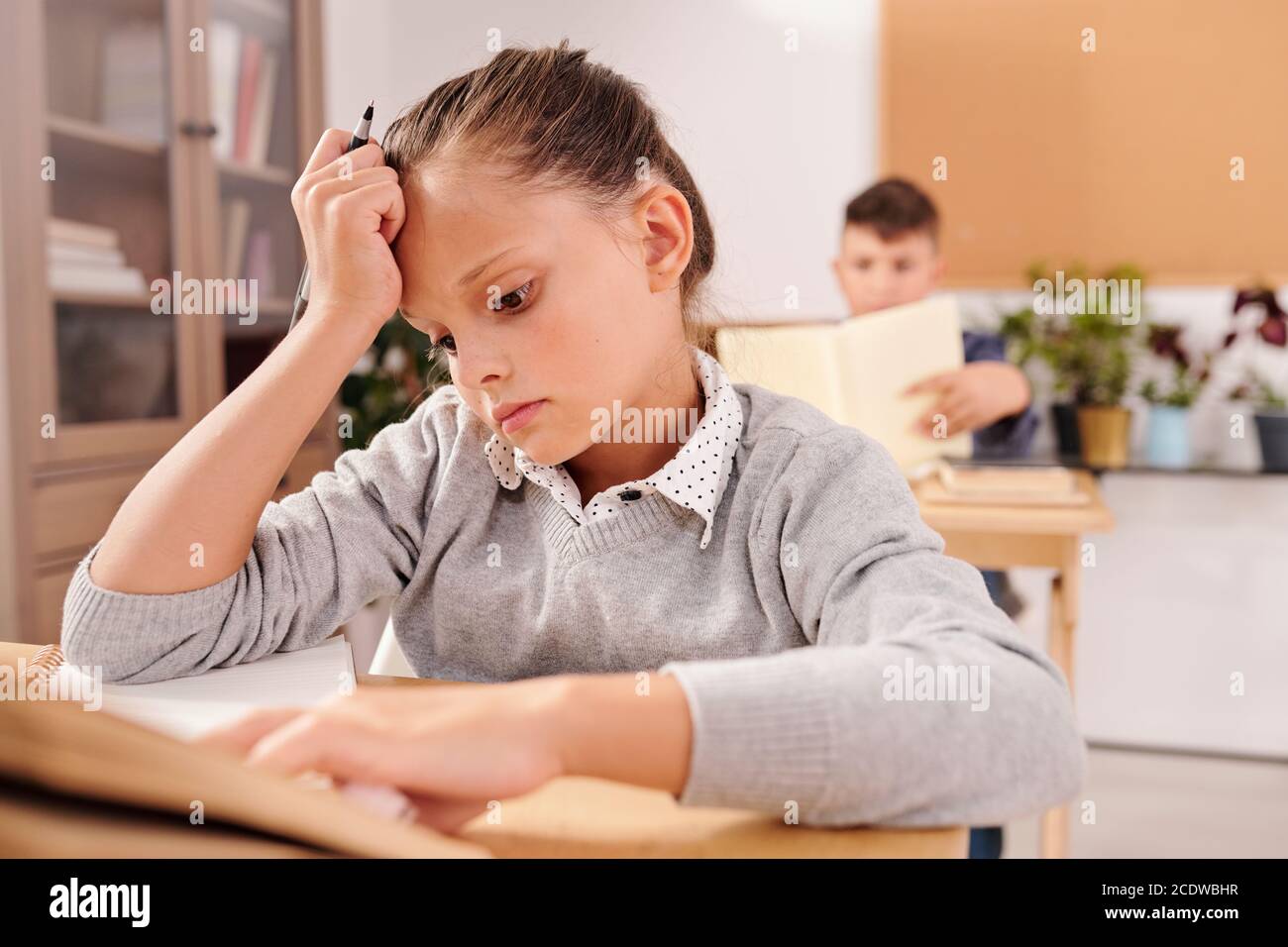 Carino schoolgirl serio che guarda la domanda in notebook e pensare di risposta Foto Stock