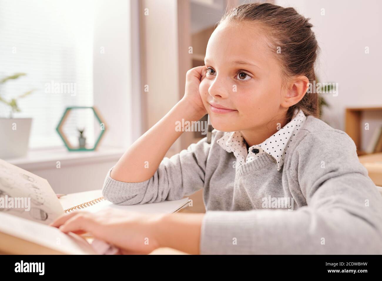 Sorridente studentessa intelligente con libro aperto guardando attraverso le domande su lavagna Foto Stock