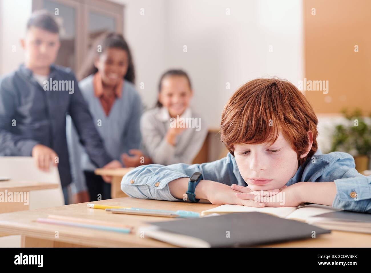 Scolaro annoiato che tiene il mento e le mani sul copybook mentre legge note Foto Stock