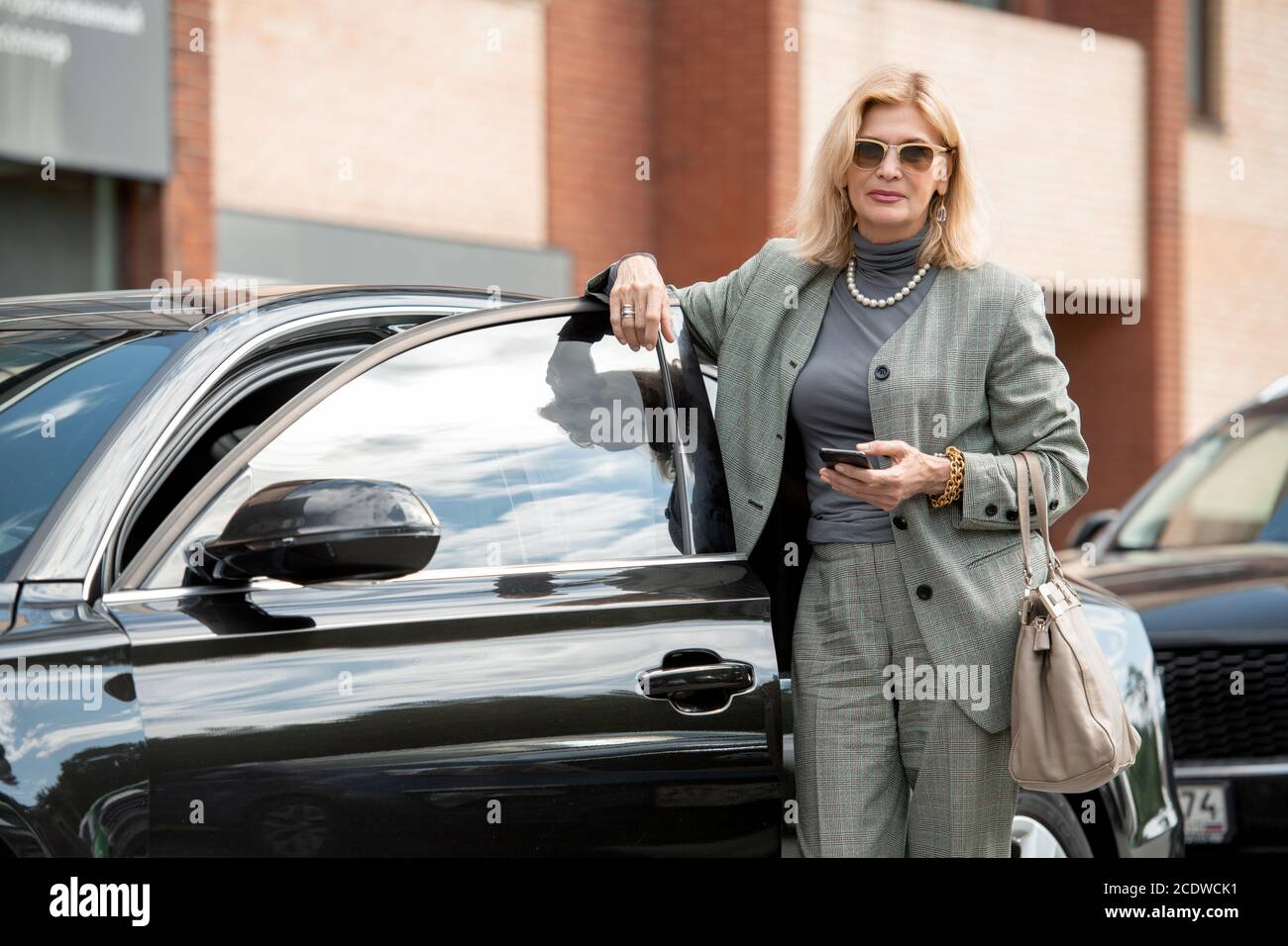 Elegante donna d'affari matura o agente in occhiali da sole, tuta e collana di perle Foto Stock