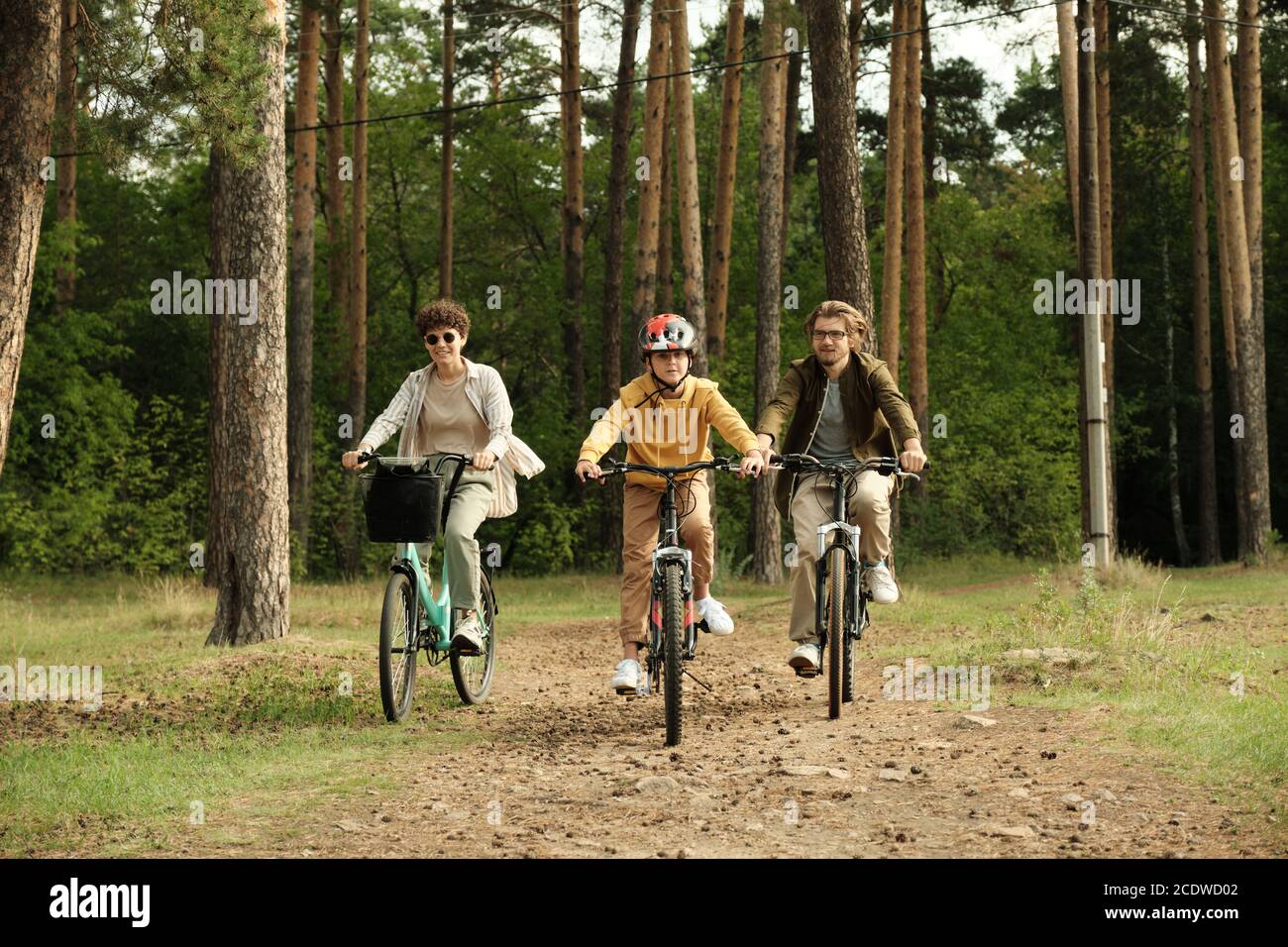 Felice famiglia di giovane marito, moglie e figlio a cavallo biciclette lungo il percorso forestale Foto Stock