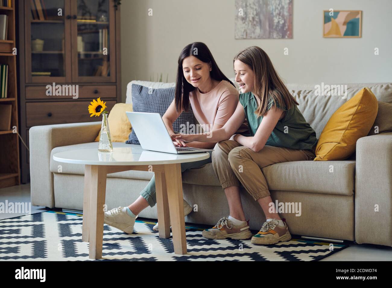 Ridendo l'adolescente e la sua madre felice seduta sul divano dentro parte anteriore del computer portatile Foto Stock