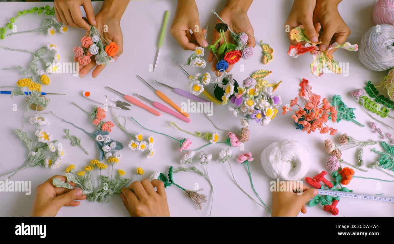 Incredibile vista dall'alto gruppo di donne lavoro a mano con il filato per fare il prodotto fatto a mano, colorato piccolo uncinetto di fiori come regalo per la primavera decorazione, molte opere d'arte Foto Stock