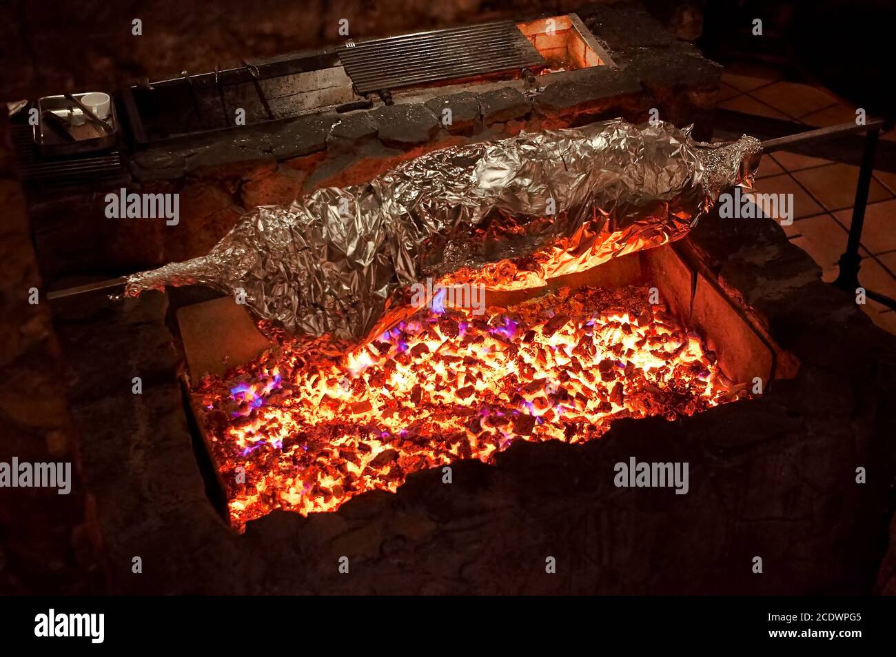 Carne alla griglia in foglio su un fuoco aperto. Corpo intero animale avvolto con lamina su una grande griglia, cucina ristorante. Foto Stock