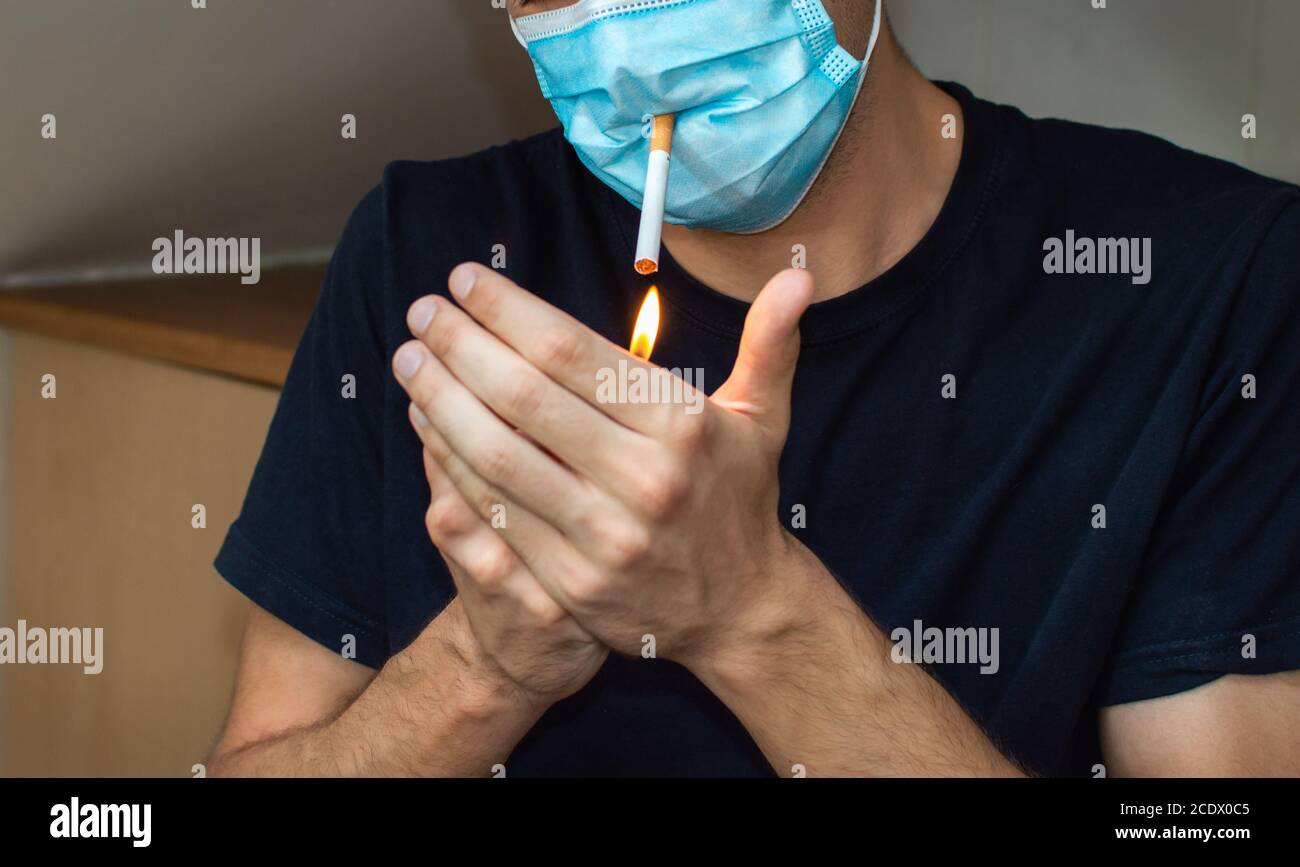 Uomo che illumina una sigaretta mentre indossa la maschera facciale. Covid concetto divertente Foto Stock
