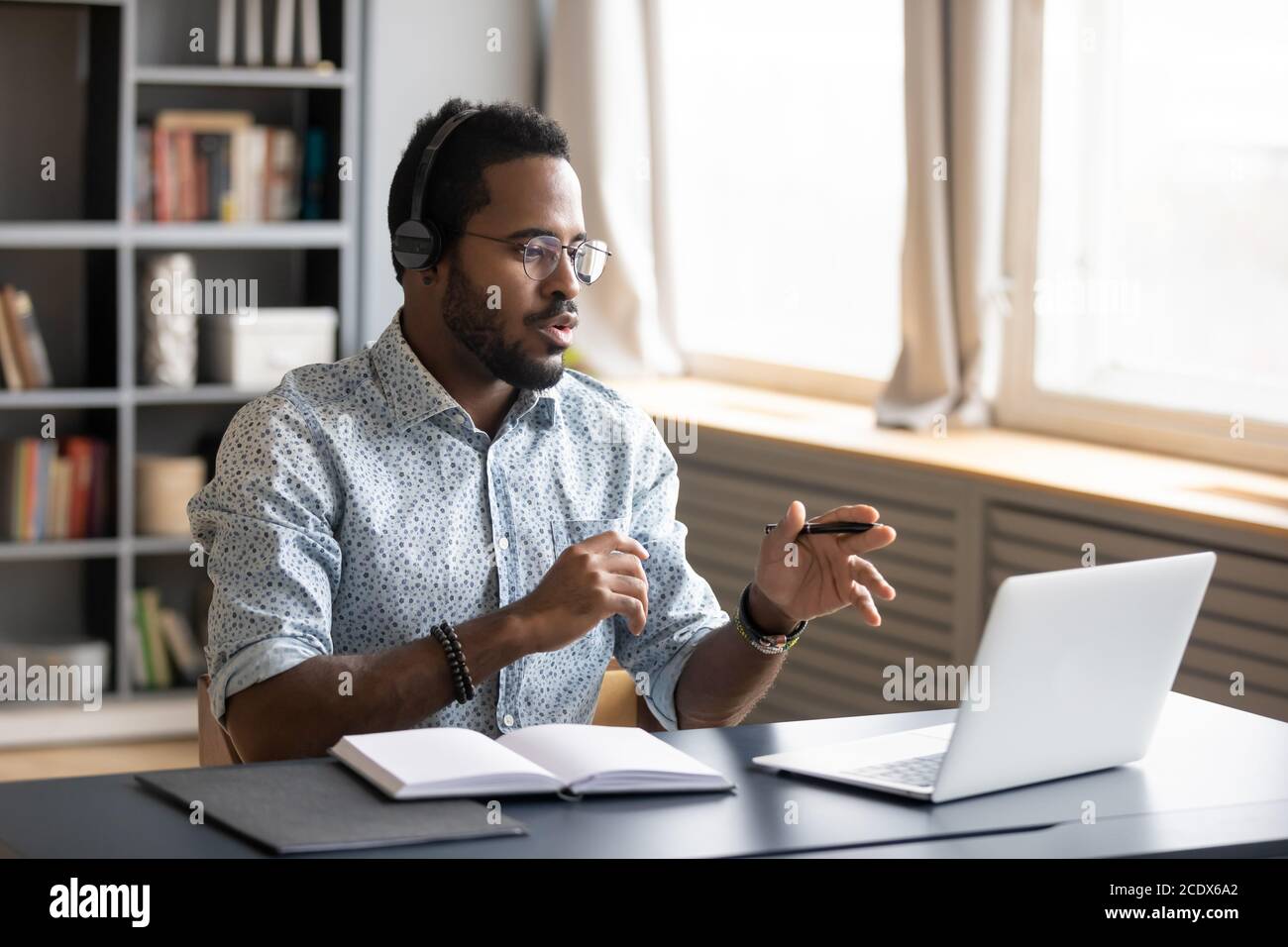 Uomo afroamericano che indossa le cuffie che parlano, usando il laptop Foto Stock