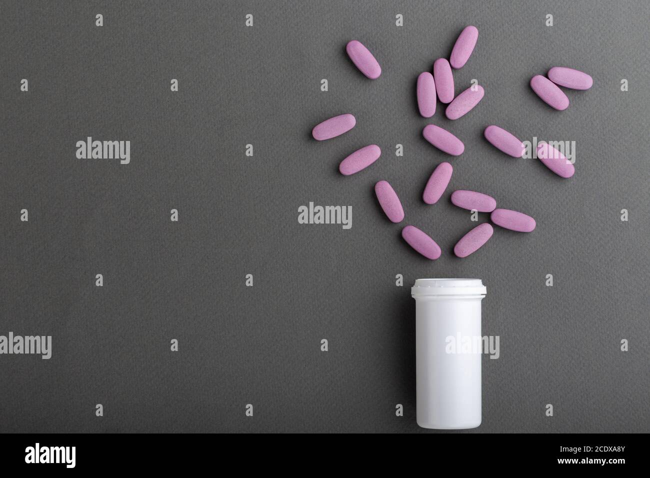 Le pillole rosa ovali vengono versate da un vaso su sfondo grigio. Spazio per il testo. Foto Stock