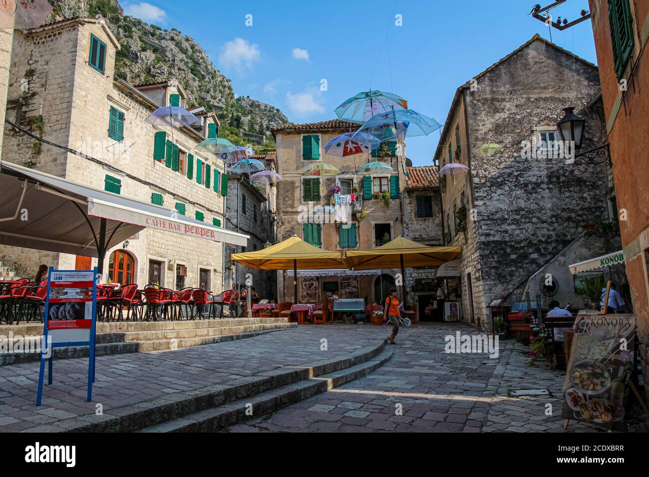 Caffè e ombrelloni volanti su una piazza nella città vecchia di Cattaro, un sito patrimonio dell'umanità dell'UNESCO, Montenegro Foto Stock