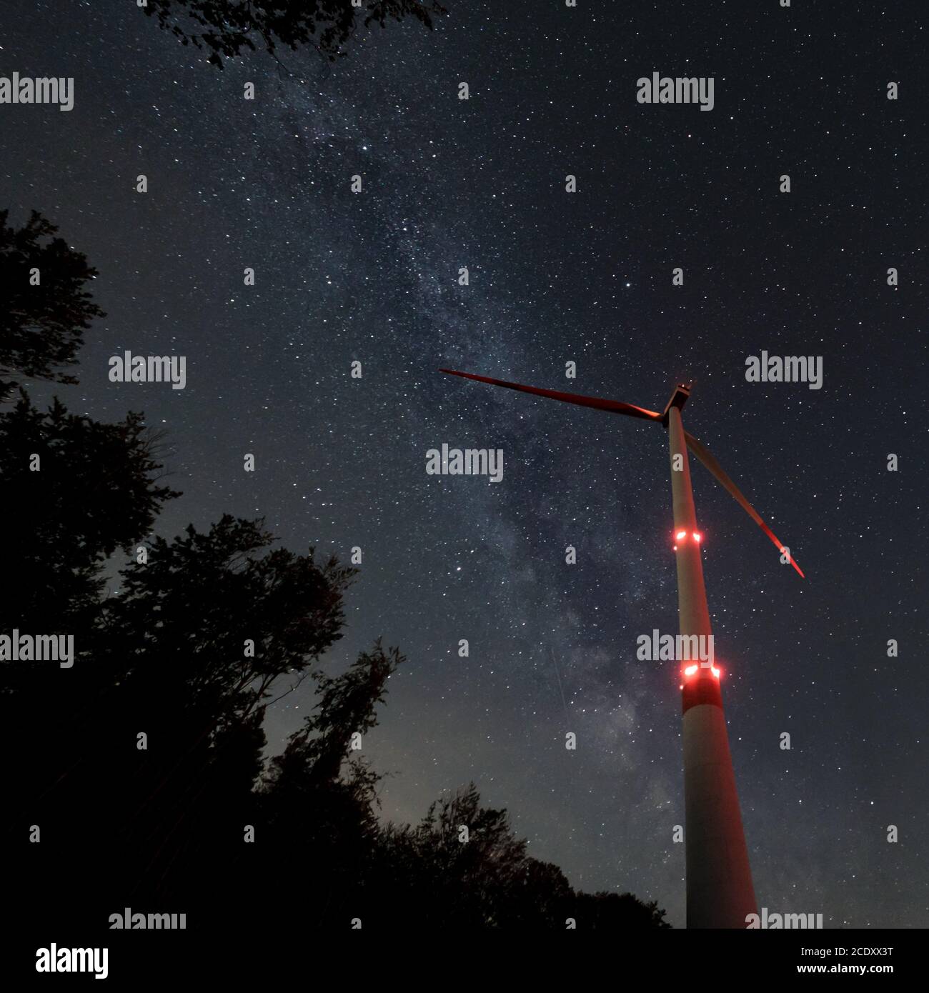 Turbina eolica industriale in mezzo alla foresta, nightshot con strada lattea e cielo stellato. Inversione di tendenza dell'energia di sostenibilità. Foto Stock