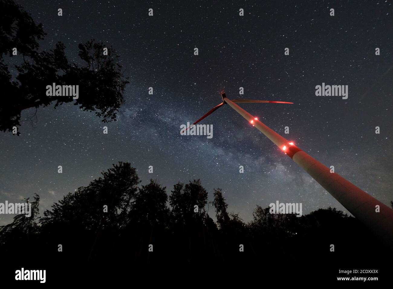 Turbina eolica industriale in mezzo alla foresta, nightshot con strada lattea e cielo stellato. Inversione di tendenza dell'energia di sostenibilità. Foto Stock