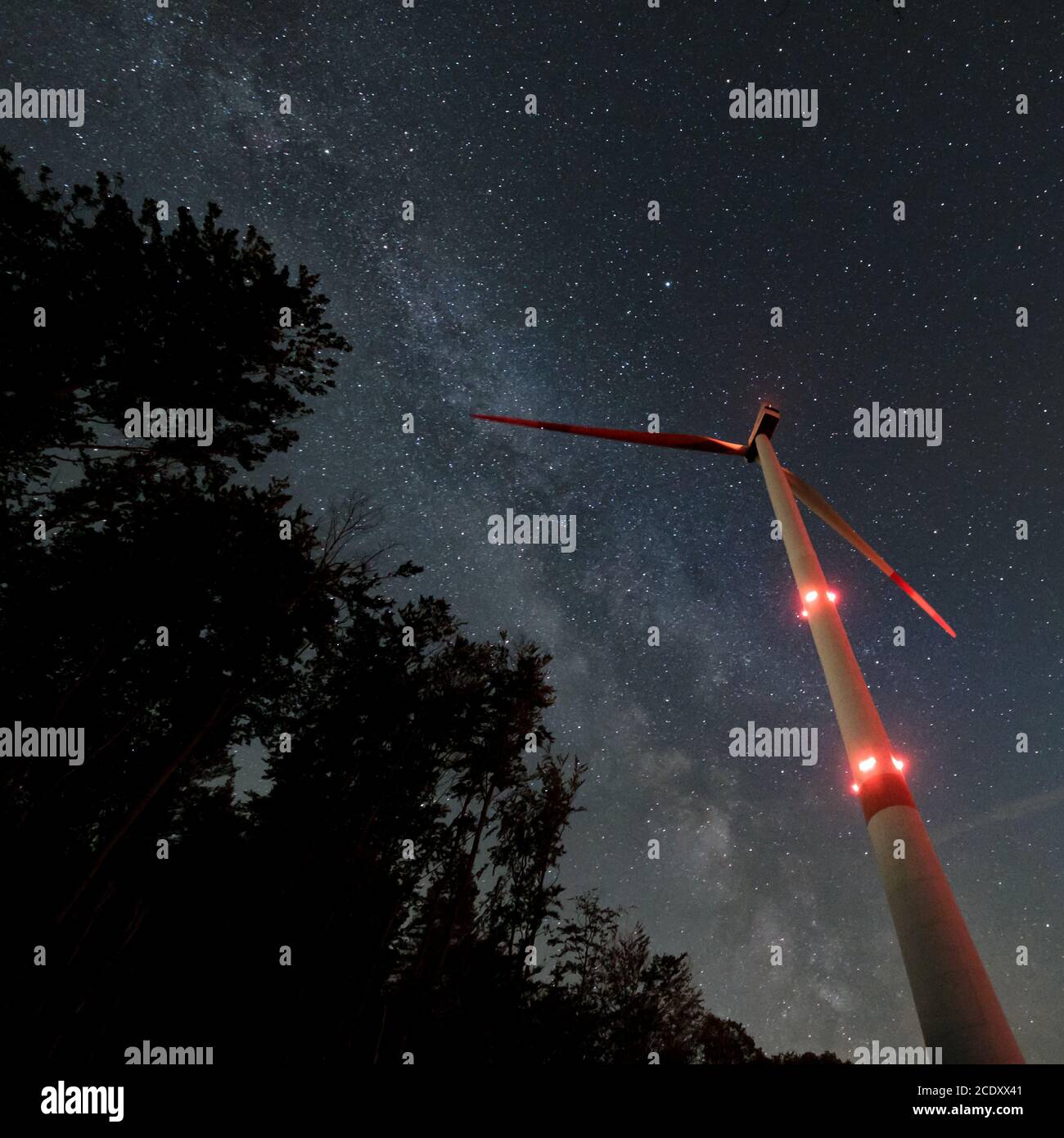 Turbina eolica industriale in mezzo alla foresta, nightshot con strada lattea e cielo stellato. Inversione di tendenza dell'energia di sostenibilità. Foto Stock