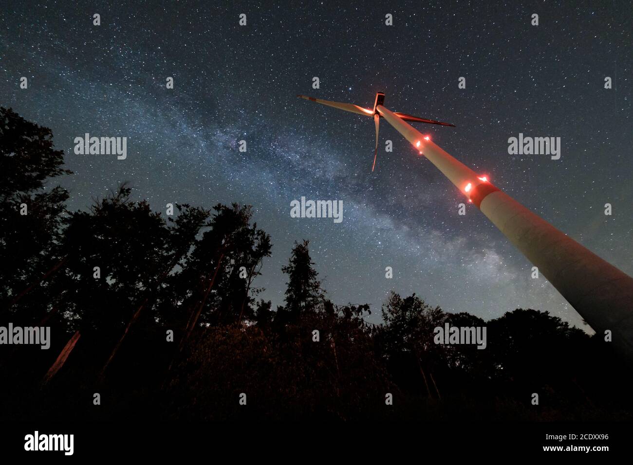 Turbina eolica industriale in mezzo alla foresta, nightshot con strada lattea e cielo stellato. Inversione di tendenza dell'energia di sostenibilità. Foto Stock