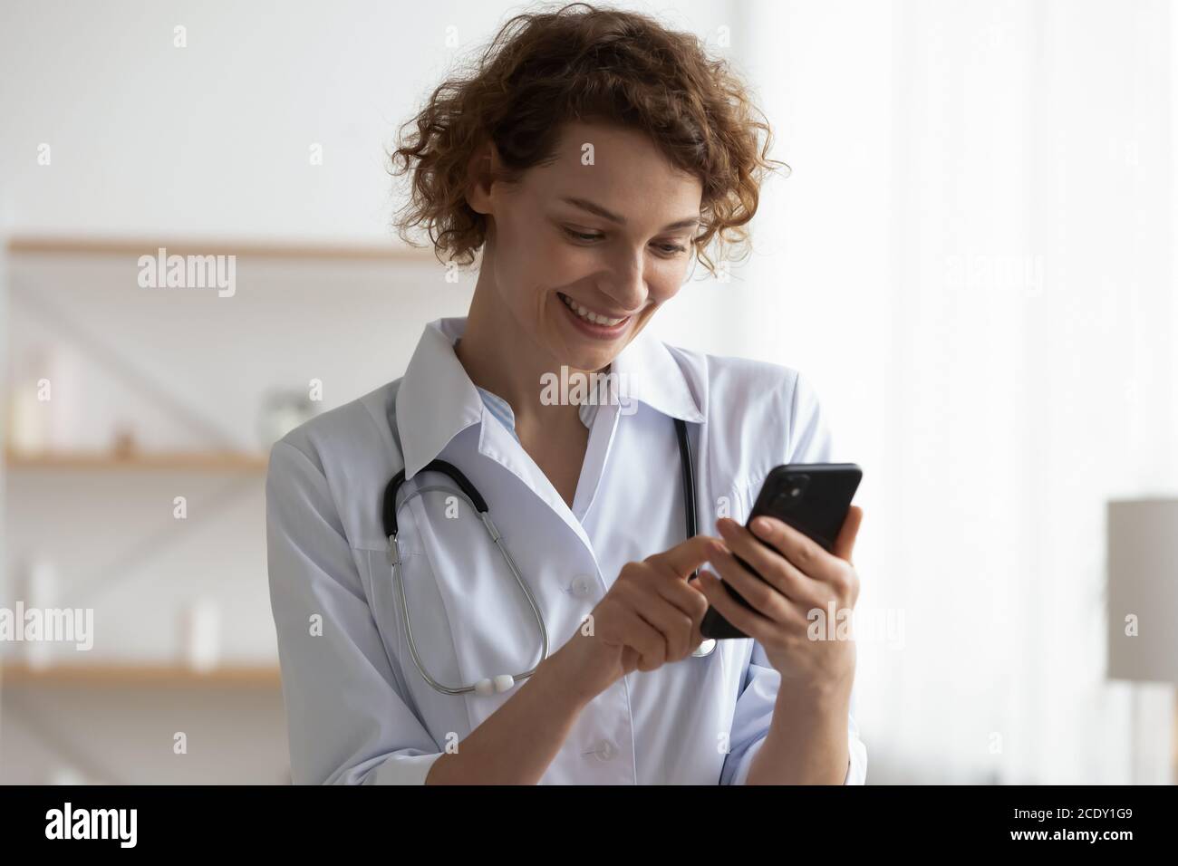 Primo piano sorridente medico donna utilizzando il telefono, guardando lo schermo Foto Stock