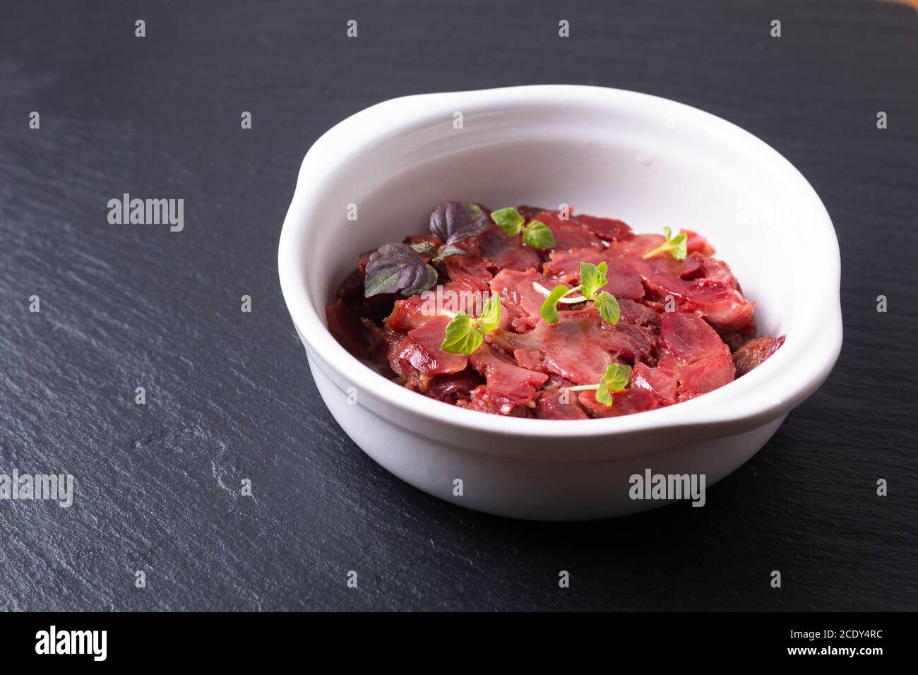 Cucina francese gesiers de poulets confits sous vide pollo gizzard Confit in tazza di ceramica bianca su tavola di ardesia nera con spazio di copia Foto Stock