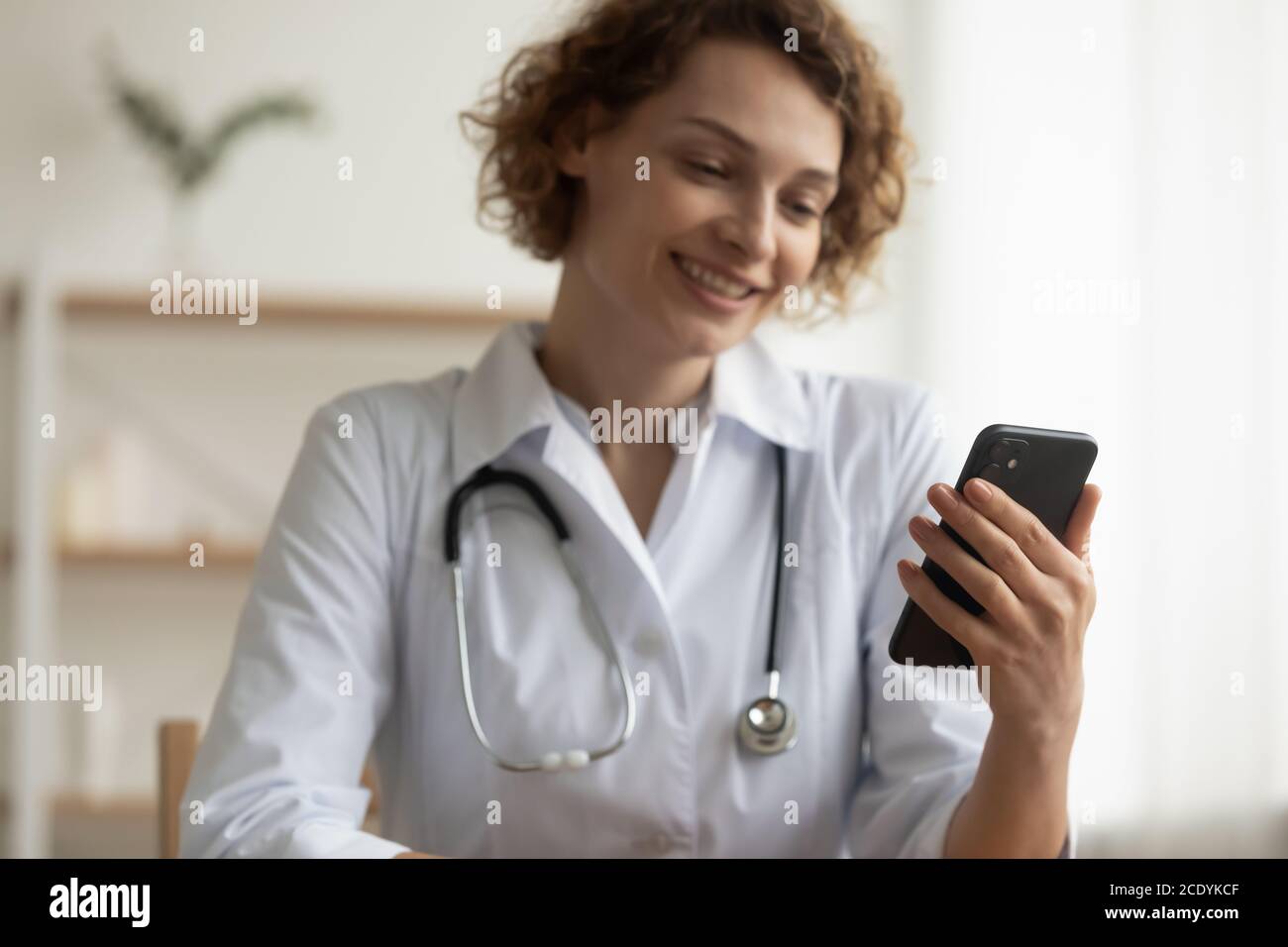 Primo piano donna sorridente dottore che effettua una videochiamata, tenendo in attesa uno smartphone Foto Stock