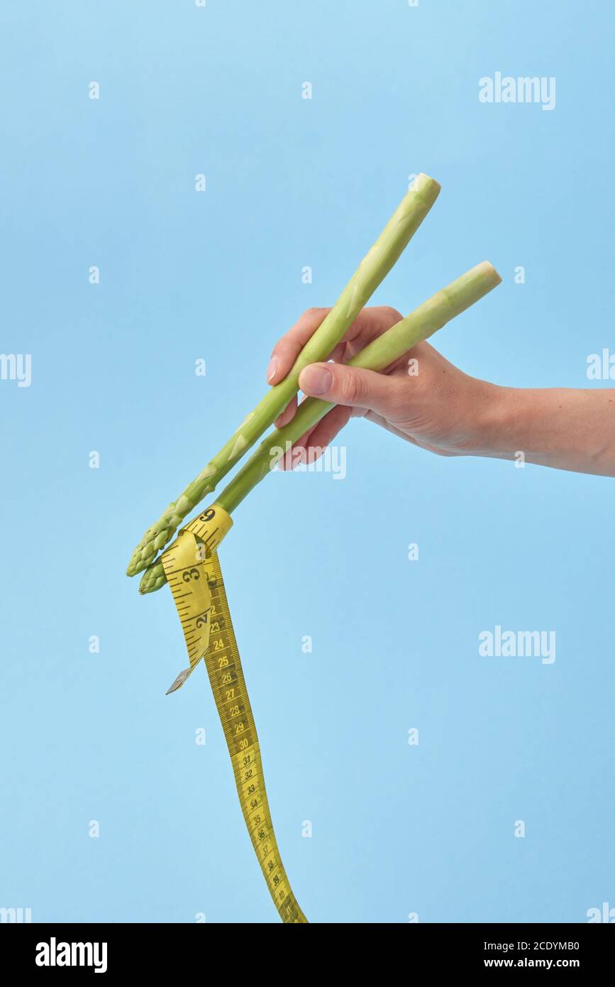 La mano femminile con bastoncini di asparagi sta prendendo nastro di misura. Foto Stock