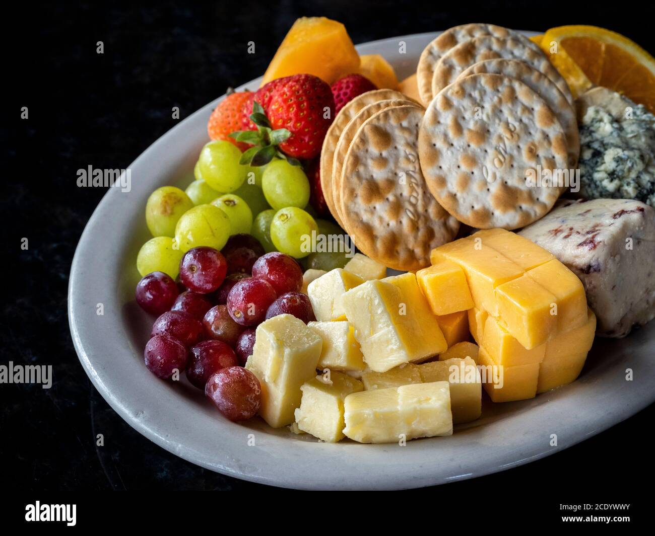 Formaggio di frutta e cracker e un piatto su un nero sfondo Foto Stock