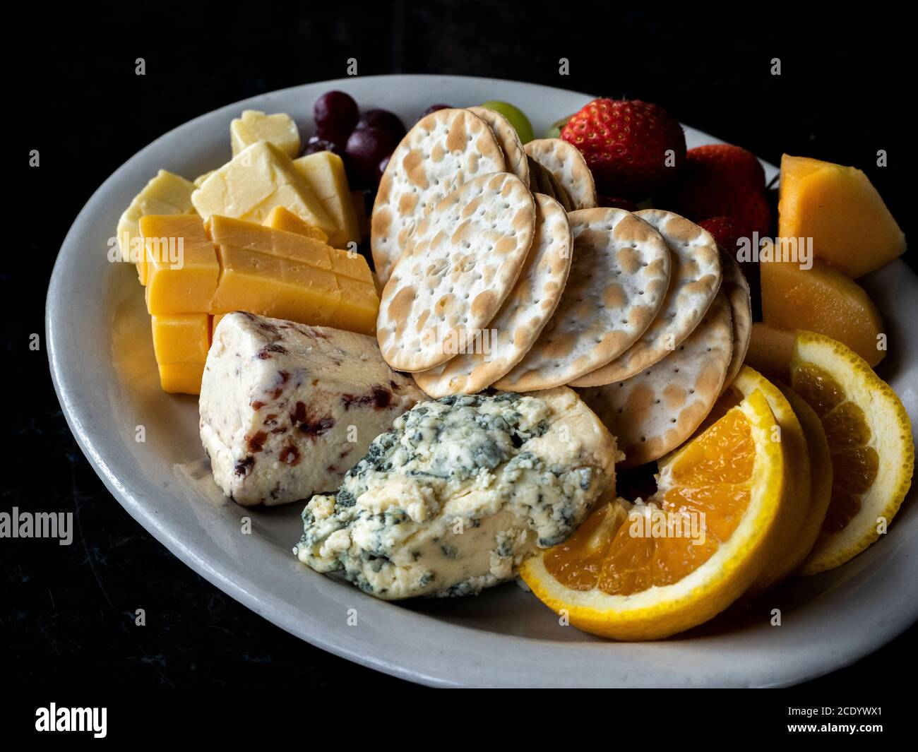 Formaggio di frutta e cracker e un piatto su un nero sfondo Foto Stock