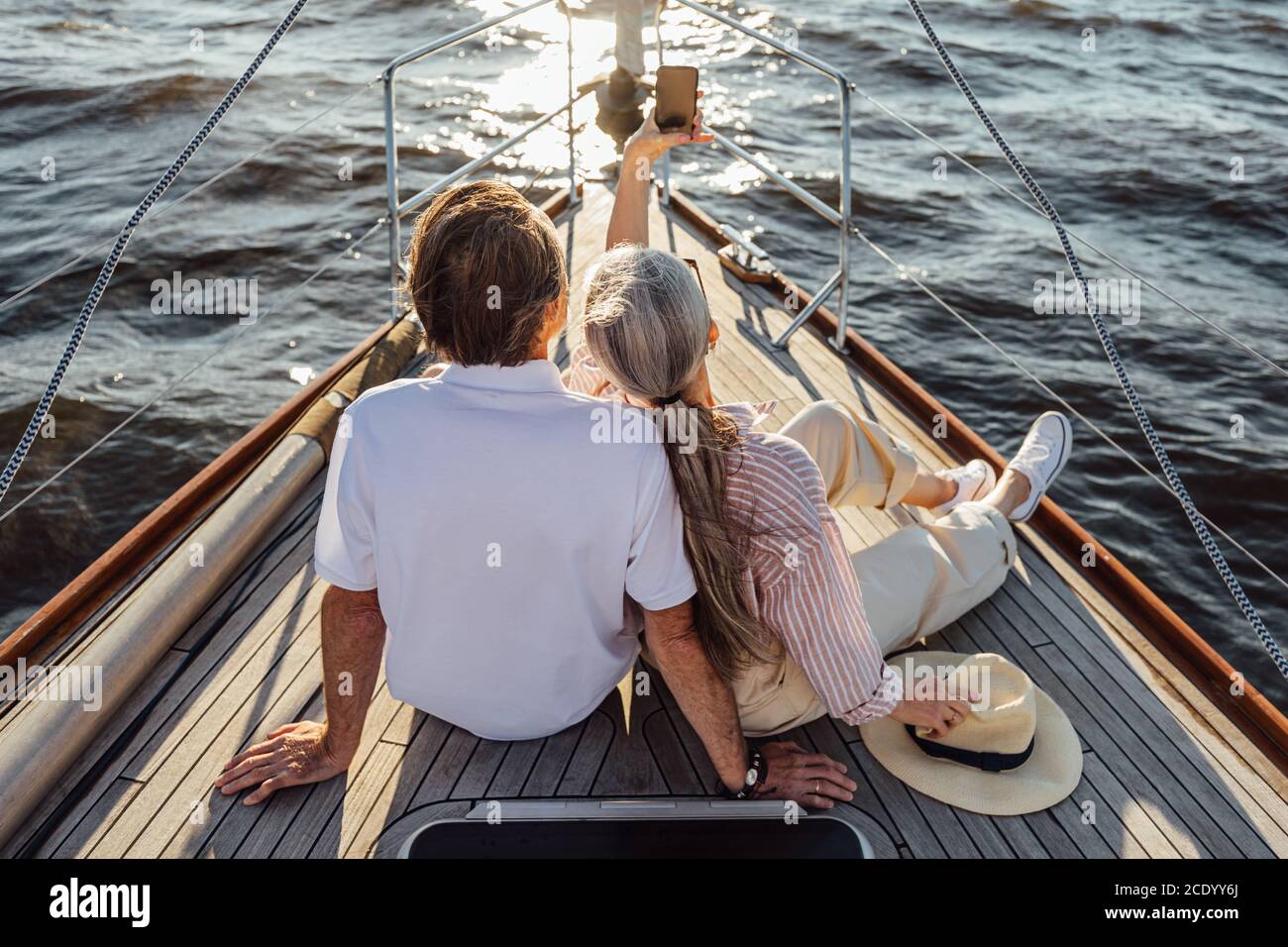 Vista posteriore di uomo anziano e donna seduto su privato yacht e prendendo selfie con il telefono cellulare Foto Stock