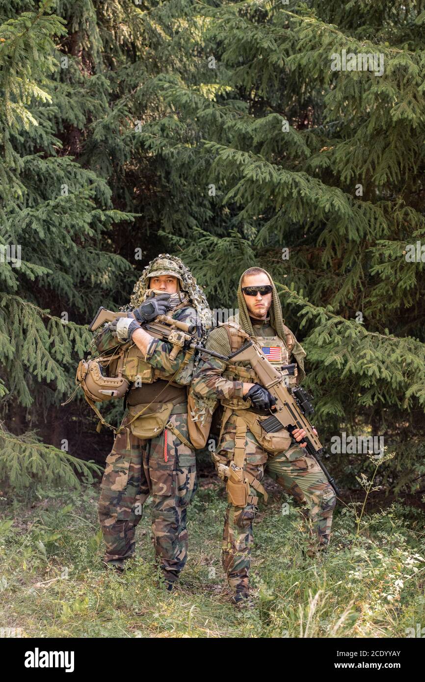 Ritratto di giovani soldati seri in abiti camouflage in piedi con arma contro alberi di foresta Foto Stock