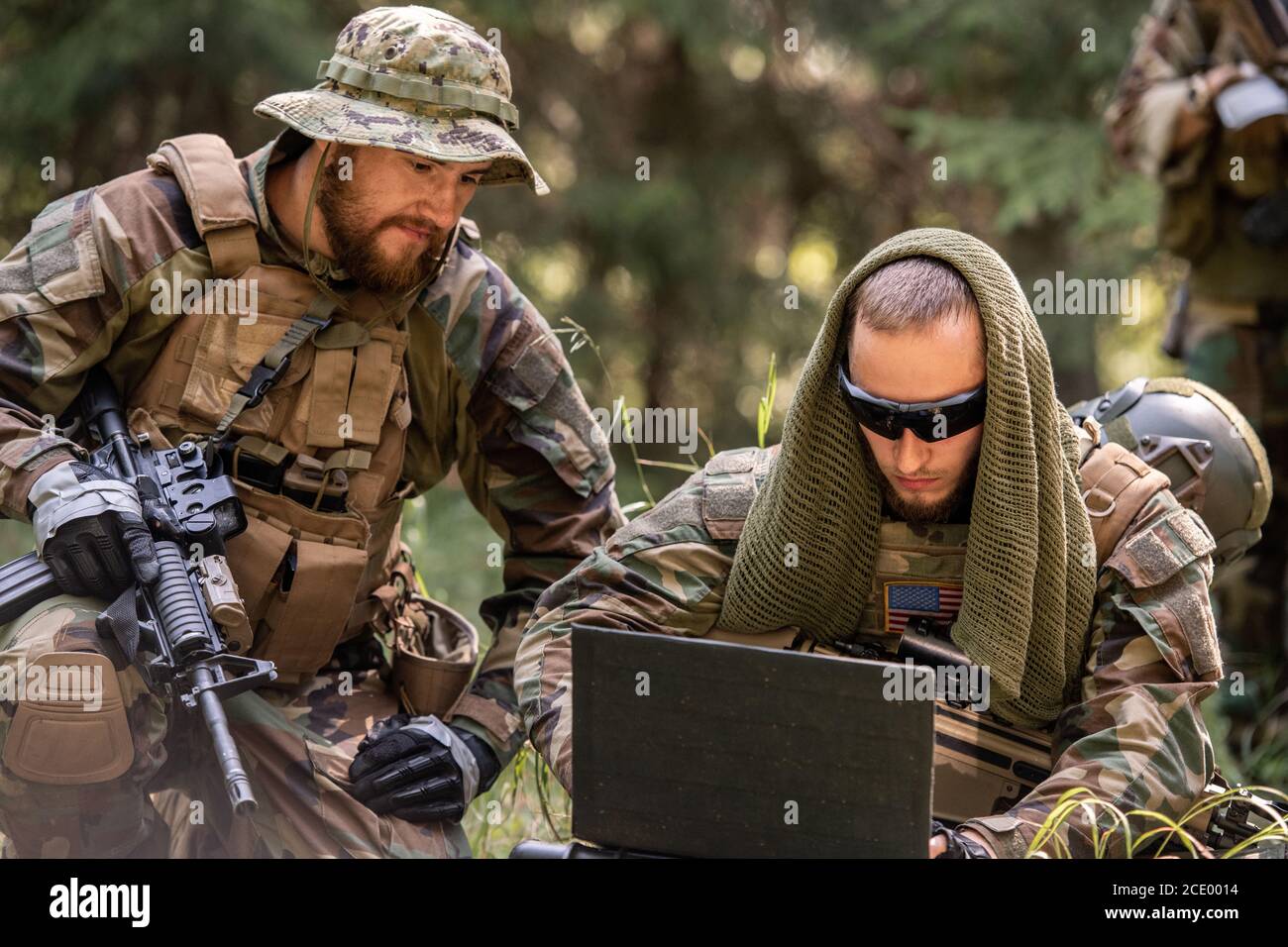 Soldati americani dell'esercito in abiti da camuffamento seduti a terra e. utilizzo del computer portatile durante la discussione di ulteriori azioni Foto Stock