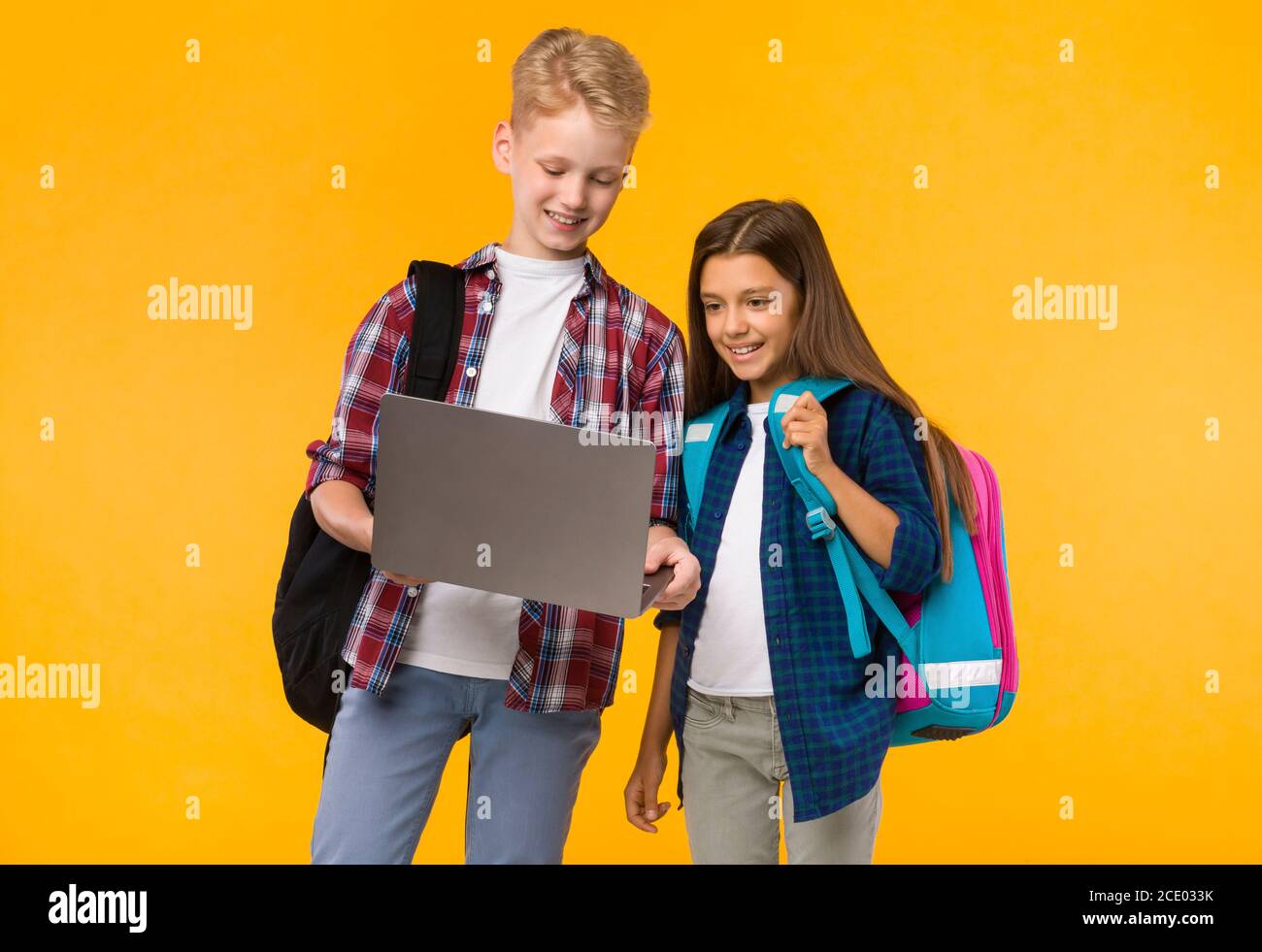 Ragazza felice e ragazzo che tengono il laptop allo studio giallo Foto Stock