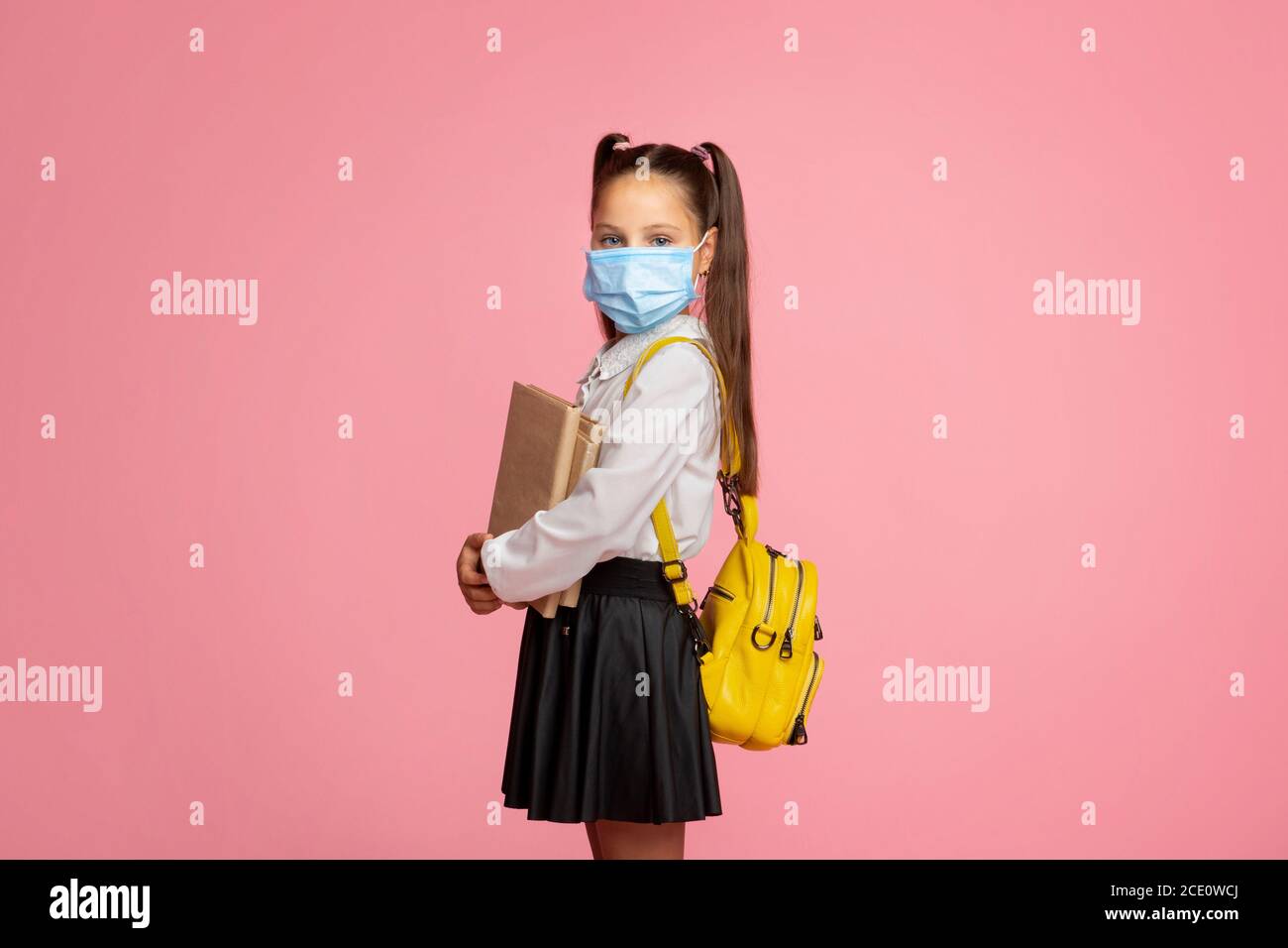 Scuola durante la quarantena. Bambino piccolo in uniforme con libri, zaino e maschera protettiva Foto Stock