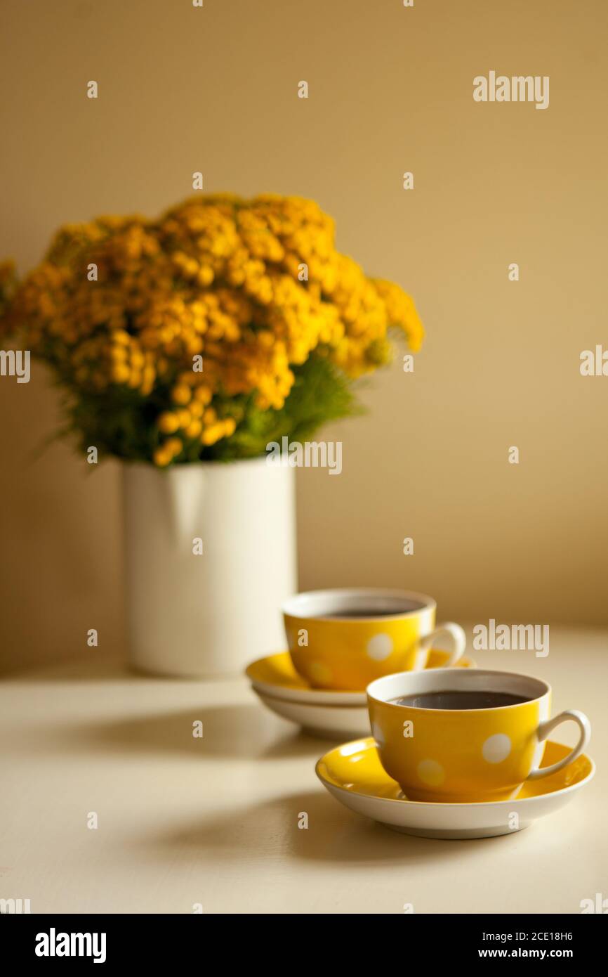 Due tazze di caffè gialle su sfondo bianco, pausa caffè e aggiunta di caffeina concetto. Fiori gialli sul tavolo Foto Stock