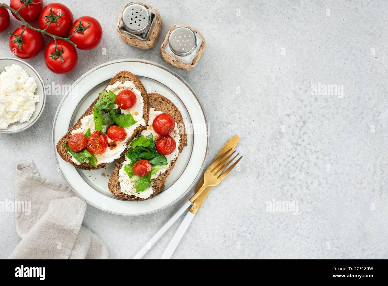 Bruschetta italiana sana con ricotta, lattuga romena e pomodori ciliegini arrostiti. Vista dall'alto del tavolo, spazio di copia Foto Stock