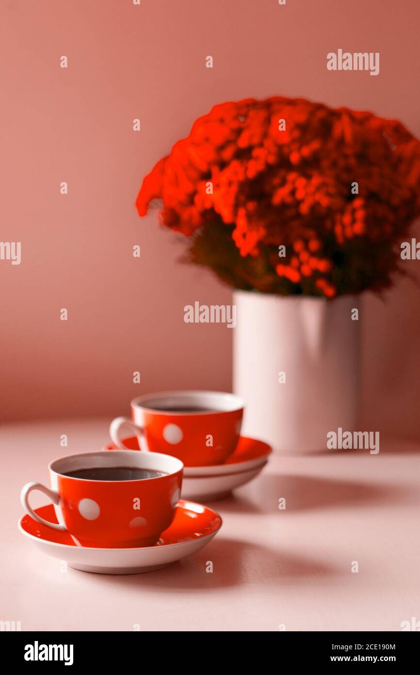 Due tazze da caffè rosse su sfondo bianco, pausa caffè e dipendenza da caffeina. Fiori rossi sul tavolo Foto Stock