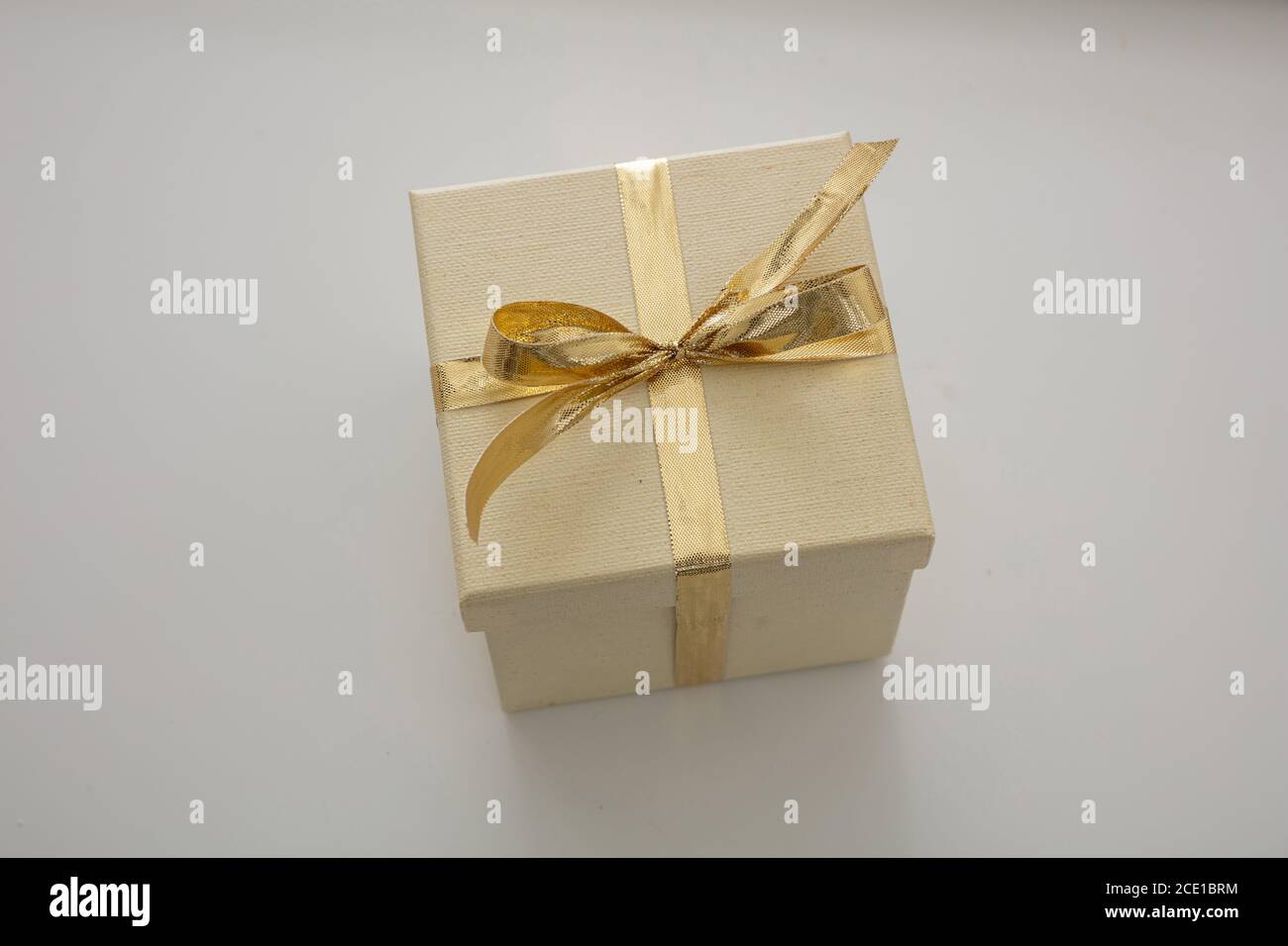 Sorpresa con il concetto attuale. Confezione regalo chiusa beige con nastro di colore oro lucido isolato su sfondo grigio. Sopra, primo piano, angolo alto v Foto Stock
