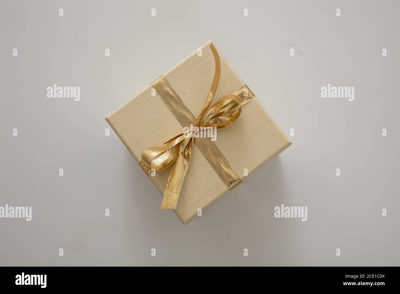 Sorpresa con il concetto attuale. Confezione regalo chiusa beige con nastro di colore oro lucido isolato su sfondo grigio. Vista dall'alto. Foto Stock