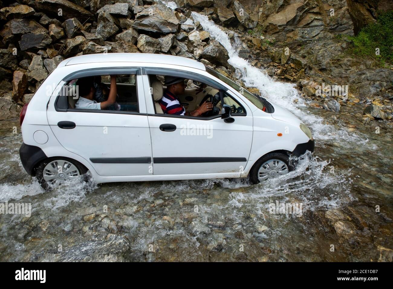 Un'auto bianca con passeggeri che attraversano una pericolosa cascata Una strada in Sikkim in India Foto Stock