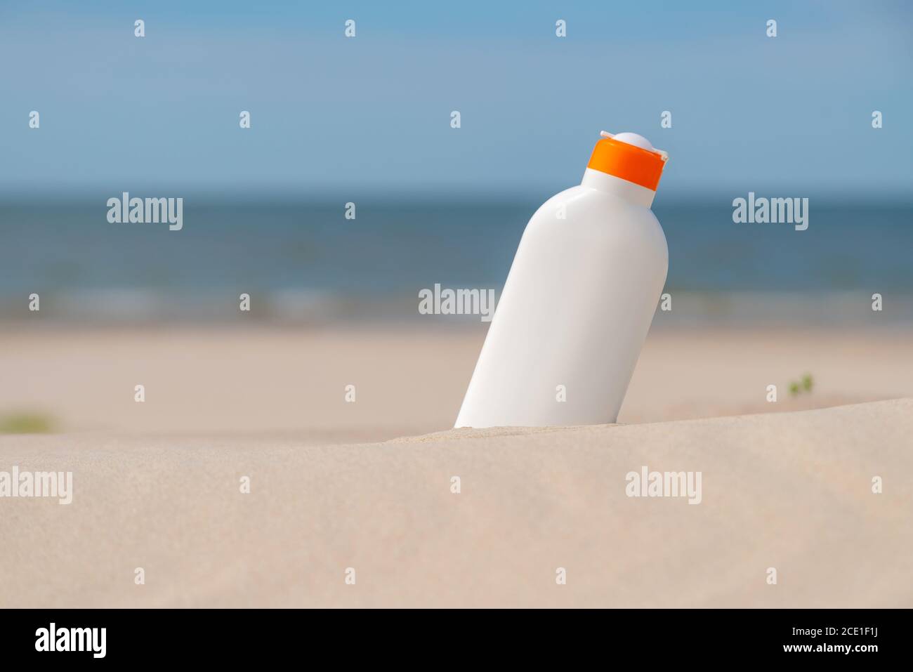 Crema di protezione solare nella sabbia in una giornata di sole in spiaggia. Bottiglia bianca crema solare protezione da scottature. Nessuno. Foto Stock