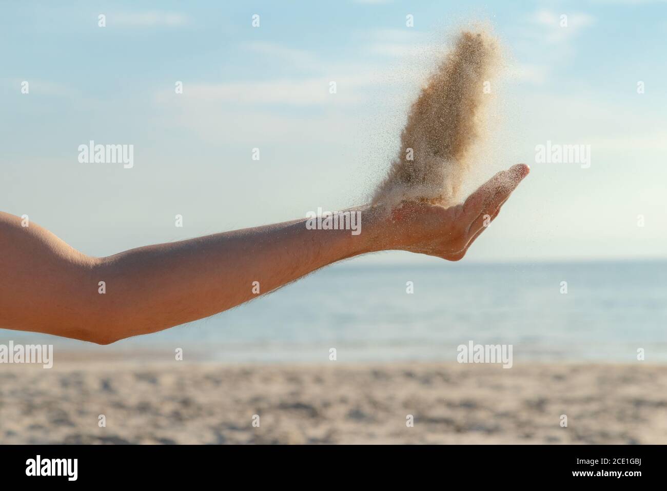 Primo piano di sabbia che si riversano dalla mano sulla spiaggia in una soleggiata giornata estiva. Giocare con la sabbia in vacanza. Foto Stock