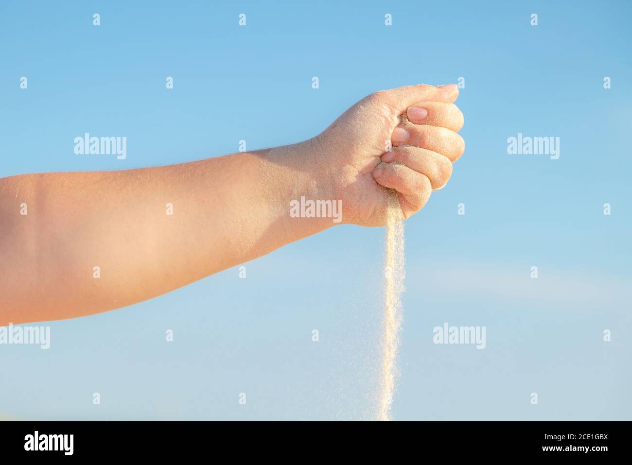 Primo piano di sabbia che si riversano dalla mano sulla spiaggia in una soleggiata giornata estiva. Giocare con la sabbia in vacanza. Foto Stock
